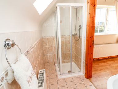A bathroom with a tiled shower enclosure a towel on a ring and a wooden door leading to a room with a window and radiator at Fern View House Beaufort near Killorglin County Kerry