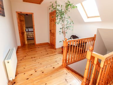 A wooden floor hallway with doors a potted plant a chair and a stair railing at Fern View House in Beaufort near Killorglin County Kerry