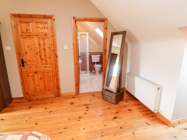 A wooden floor room with two wooden doors one leading to a bathroom a standing mirror and a white radiator at Fern View House Beaufort near Killorglin County Kerry