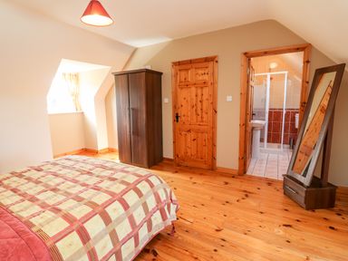 A bedroom with a bed covered by a patterned quilt a wardrobe a mirror and an en suite bathroom at Fern View House in Beaufort near Killorglin County Kerry