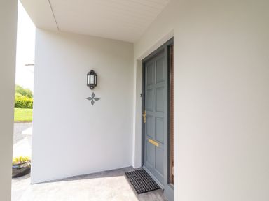 A front porch area with a closed gray door a black wall-mounted lantern and a black doormat at Fern View House in Beaufort near Killorglin County Kerry
