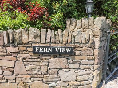 A stone wall with a sign reading FERN VIEW and greenery behind the wall with a black metal gate at Fern View House in Beaufort near Killorglin County Kerry