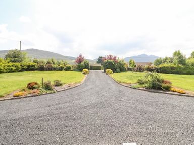 A gravel driveway with grass and shrubbery on both sides and mountains in the background at Fern View House in Beaufort near Killorglin County Kerry