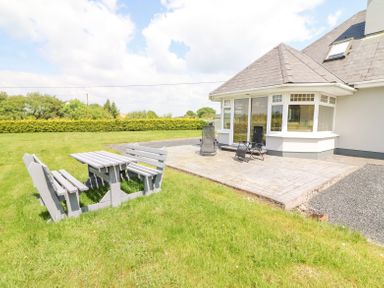 A house with a patio and outdoor chairs next to a wooden table and benches on the grass at Fern View House in Beaufort near Killorglin County Kerry