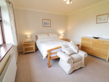 A bedroom with a double bed two wooden bedside tables a wooden dresser and an armchair at Brynteg in Llwyngwril