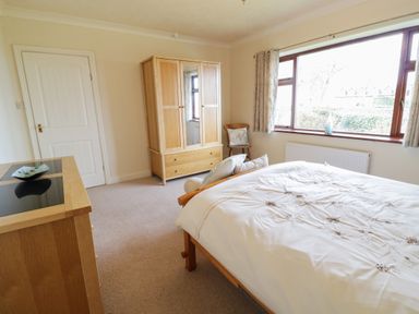 A bedroom with a bed a wardrobe a chest of drawers a chair and a window at Brynteg in Llwyngwril