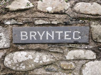A stone wall with a metal sign reading BRYNTEC at Brynteg Llwyngwril