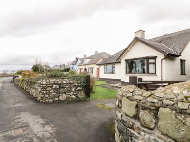 A row of houses with stone walls and a sidewalk along a curved road at Brynteg in Llwyngwril