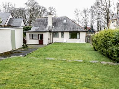 A house with a gray roof and white walls behind a green lawn with shrubs and trees at Brynteg in Llwyngwril
