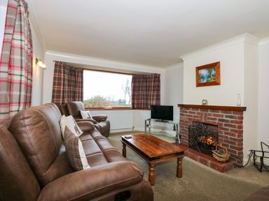A living room with brown leather sofas a wooden coffee table a brick fireplace and a television at Brynteg in Llwyngwril