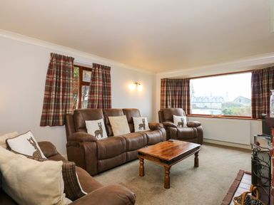 A living room with brown leather sofas cushions a wooden coffee table large window with plaid curtains at Brynteg in Llwyngwril
