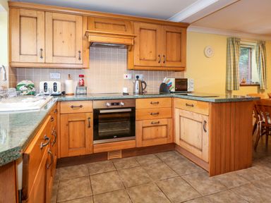 A kitchen with wooden cabinets green countertops an oven a microwave kettle and a sink at Brynteg in Llwyngwril