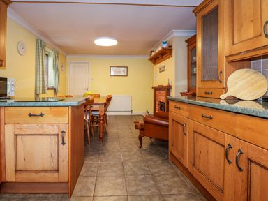 A kitchen with wooden cabinets a dining table with chairs and a leather armchair at Brynteg in Llwyngwril