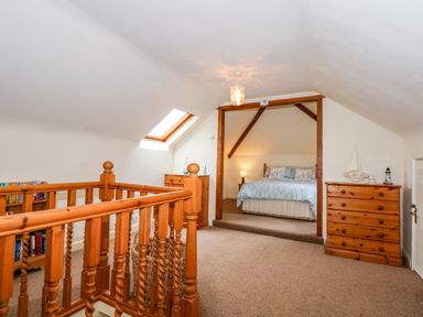 A bedroom with a wooden railing in the foreground a double bed with bedside lamp wooden dressers and a skylight window at Brynteg in Llwyngwril