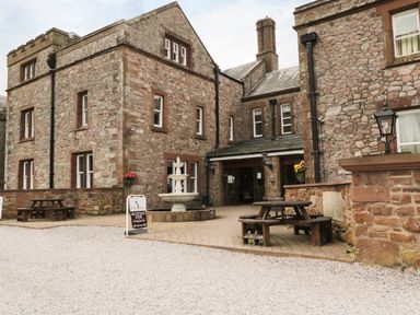 A stone building with windows and outdoor seating near a fountain with a sign saying reception and bar at Irton Hall near Wastwater