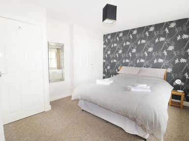 A bedroom with a double bed two bedside tables a floral wallpaper and a wall mirror at William Court Cottage in Irton Hall near Wastwater