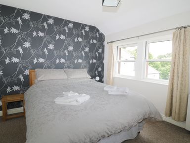 A bedroom with a bed, bedside table, patterned wallpaper, and two windows with curtains at William Court Cottage in Irton Hall near Wastwater