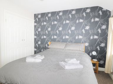 A bedroom with a double bed with towels on it a bedside table with a lamp and a floral patterned wallpaper at William Court Cottage Irton Hall near Wastwater