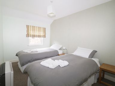 A bedroom with two single beds with gray bedding a bedside table lamp and a window with striped blinds at William Court Cottage Irton Hall near Wastwater
