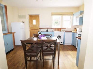A kitchen with blue cabinets a dining table with chairs a white fridge and washing machine at William Court Cottage Irton Hall near Wastwater