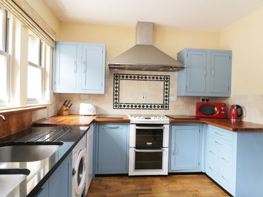 A kitchen with blue cabinets wooden countertops a white stove a red microwave and kettle at William Court Cottage Irton Hall near Wastwater
