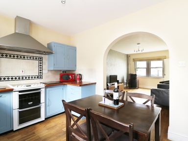 A kitchen with blue cabinets and a wooden table with chairs connected to a living room with a television at William Court Cottage Irton Hall near Wastwater