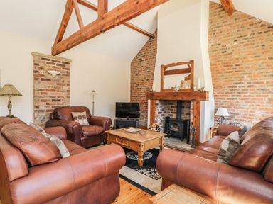 A living room with leather sofas a wooden coffee table a fireplace with wood burner and exposed brick walls at Wheelhouse Cottage in Sowerby outskirts of Thirsk