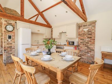 A kitchen with wooden dining table and six chairs set with plates and bowls at Wheelhouse Cottage in Sowerby outskirts of Thirsk