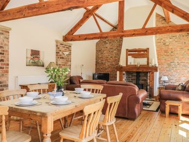 A dining area with a wooden table set with dishes and a living area with leather sofas and a fireplace at Wheelhouse Cottage in Sowerby outskirts of Thirsk