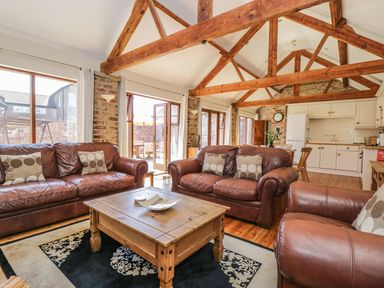 A living room with brown leather sofas a wooden coffee table and exposed wooden beams at Wheelhouse Cottage in Sowerby outskirts of Thirsk