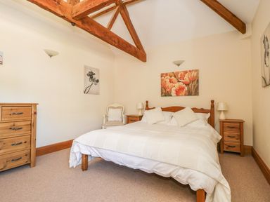 A bedroom with a bed with white bedding two wooden bedside tables and a wooden chest of drawers at Wheelhouse Cottage in Sowerby outskirts of Thirsk