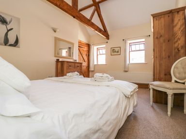 A bedroom with a bed, wooden dresser, wooden wardrobe, chair, mirror, and windows at Wheelhouse Cottage in Sowerby outskirts of Thirsk
