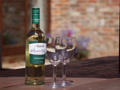 A bottle of Chardonnay and two empty wine glasses on a wooden table outdoors at Wheelhouse Cottage in Sowerby outskirts of Thirsk
