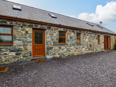 A stone exterior wall of a building with wooden doors and windows and a gravel ground at Cefn-Yr-Efail in Golan near Porthmadog