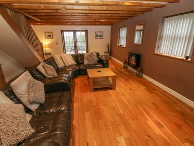 A living room with a brown leather sofa and cushions wooden coffee table wooden floor and ceiling beams at Cefn-Yr-Efail in Golan near Porthmadog