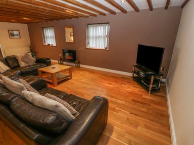 A living room with leather sofas a wooden coffee table a TV on a stand and wooden beams on the ceiling at Cefn-Yr-Efail in Golan near Porthmadog