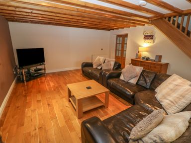 A living room with wooden floors exposed ceiling beams leather sofas a wooden coffee table and a TV on a stand at Cefn-Yr-Efail in Golan near Porthmadog