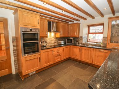 A kitchen with wooden cabinets built in oven countertop appliances and a window at Cefn-Yr-Efail in Golan near Porthmadog