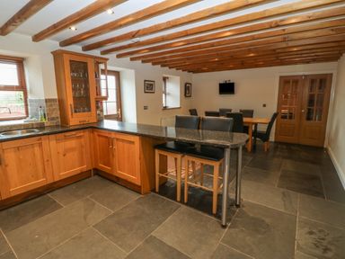 A kitchen and dining area with wooden cabinets black countertops bar stools dining table and chairs at Cefn-Yr-Efail in Golan near Porthmadog
