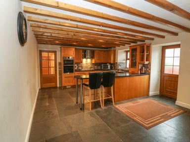 A kitchen with wooden cabinets black countertops and two stools at Cefn-Yr-Efail in Golan near Porthmadog