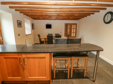 A dining room with a wooden table black chairs a clock on the wall and a granite countertop with high stools Cefn-Yr-Efail Golan near Porthmadog