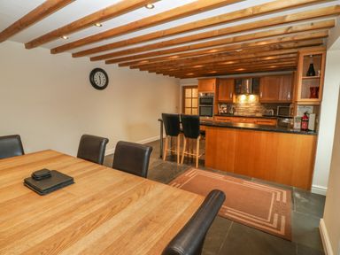A kitchen and dining area with wooden table, black chairs, a clock on the wall, and wooden beams on the ceiling at Cefn-Yr-Efail in Golan near Porthmadog