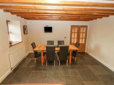 A dining room with a wooden table and six black chairs under wooden ceiling beams at Cefn-Yr-Efail in Golan near Porthmadog