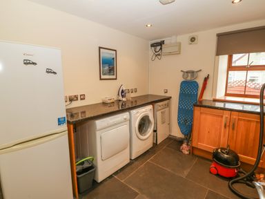 A utility room with a fridge freezer washing machine dryer ironing board and vacuum cleaner at Cefn-Yr-Efail in Golan near Porthmadog