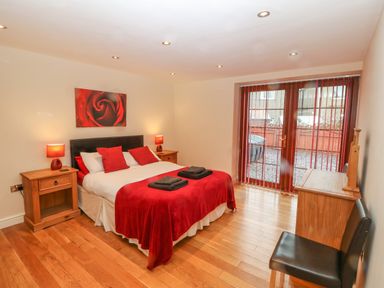 A bedroom with a bed with red pillows and blanket two wooden bedside tables and a chair near a glass door at Cefn-Yr-Efail in Golan near Porthmadog