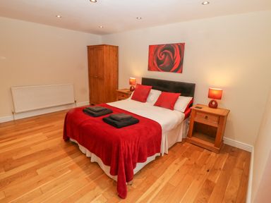 A bedroom with a double bed red bedding and pillows wooden bedside tables with lamps a wooden wardrobe and wooden floor at Cefn-Yr-Efail in Golan near Porthmadog