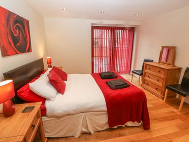 A bedroom with a double bed red pillows and blanket wooden furniture and red vertical blinds at Cefn-Yr-Efail in Golan near Porthmadog