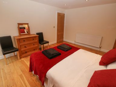 A bedroom with a bed covered in white and red bedding two black chairs a wooden dresser with a mirror and a closed wooden door at Cefn-Yr-Efail in Golan near Porthmadog