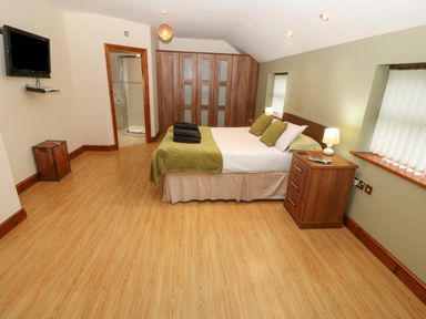 A bedroom with a bed with green pillows and blanket bedside tables with lamps a wooden wardrobe a wall-mounted TV and an en suite bathroom at Cefn-Yr-Efail in Golan near Porthmadog
