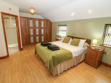 A bedroom with a double bed with green blankets and pillows two bedside tables with lamps wooden wardrobes and an ensuite bathroom at Cefn-Yr-Efail in Golan near Porthmadog